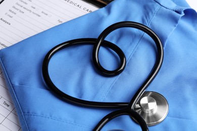 Photo of Medical uniform and stethoscope in shape of heart on paper sheets, above view