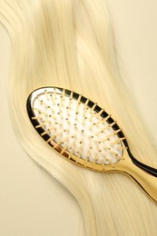Photo of Stylish brush with blonde hair strand on beige background, top view