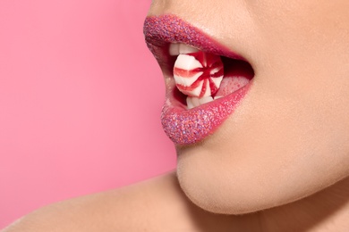 Beautiful young model with creative makeup holding candy in lips on color background