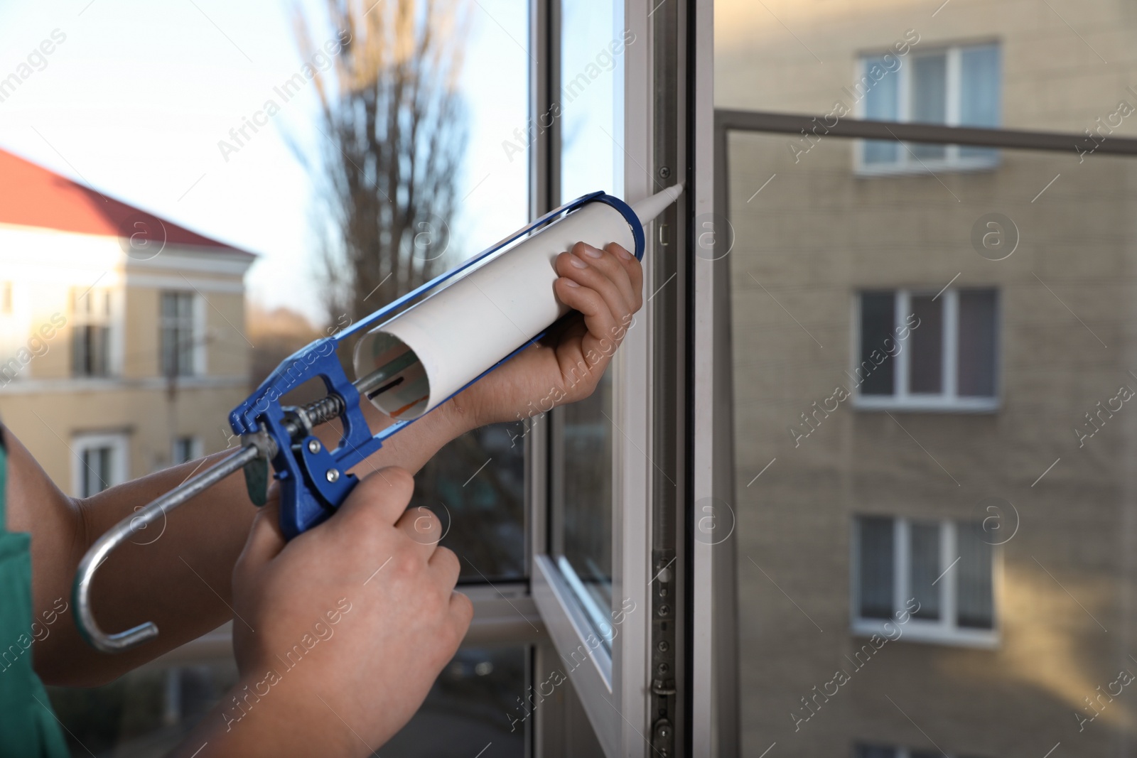 Photo of Construction worker sealing window with caulk indoors, closeup