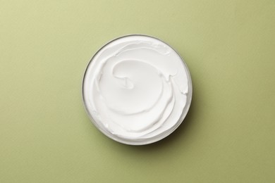 Jar of face cream on light green background, top view