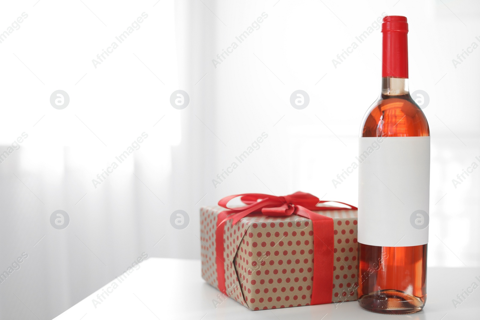 Photo of Bottle of wine and gift box on table in light room. Space for text