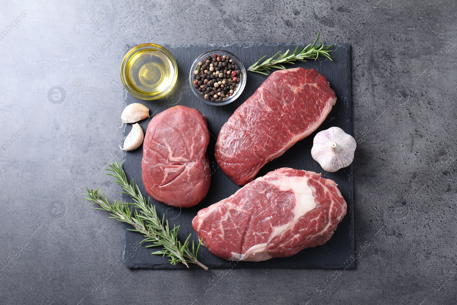 Photo of Raw beef steaks, oil and spices on grey background, top view