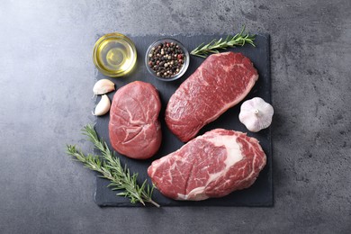 Raw beef steaks, oil and spices on grey background, top view