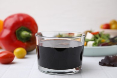 Photo of Vinegar in glass on white tiled table, closeup