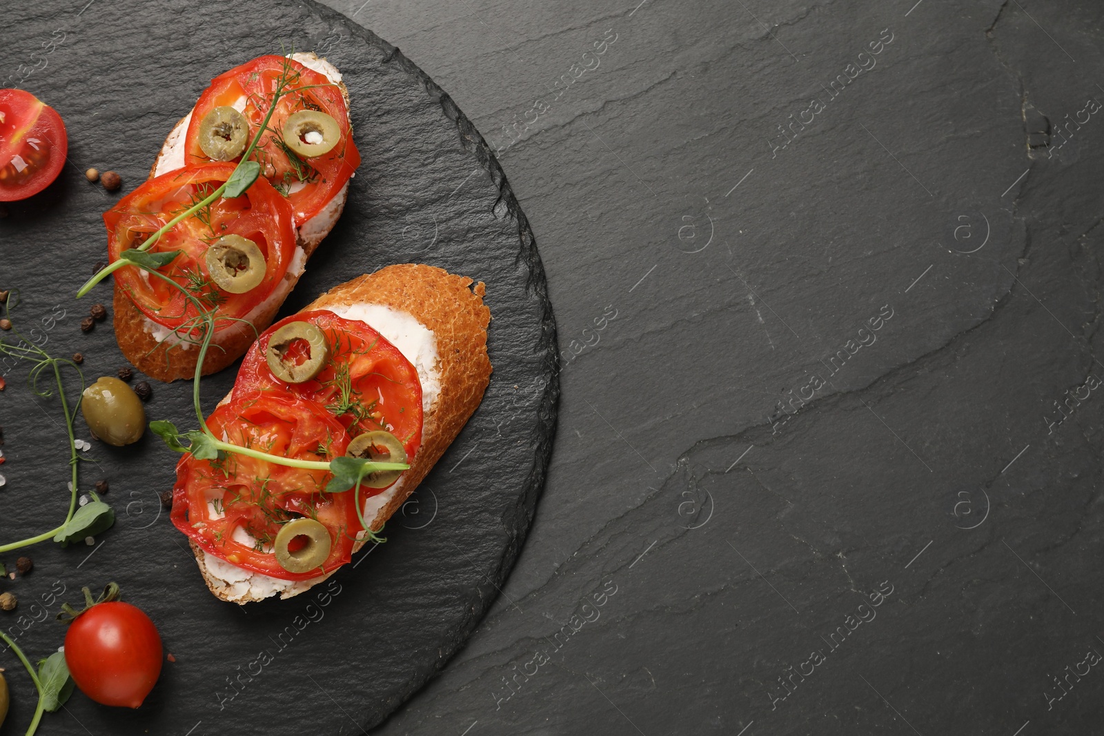 Photo of Delicious ricotta bruschettas with sliced tomatoes, olives and greens on black table, top view. Space for text