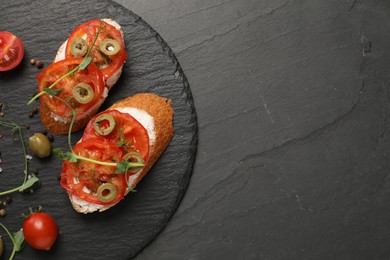 Photo of Delicious ricotta bruschettas with sliced tomatoes, olives and greens on black table, top view. Space for text