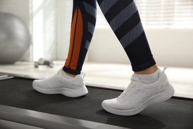 Photo of Sporty woman training on walking treadmill indoors, closeup