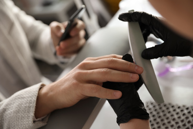 Photo of Professional manicurist filing client's nails in beauty salon, closeup