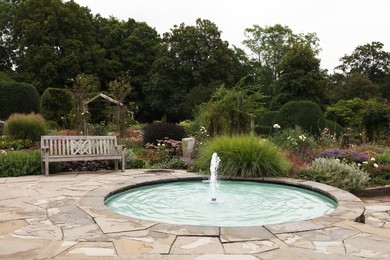 Photo of Beautiful garden with fountain, bench and green plants