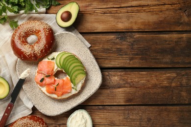 Photo of Delicious bagel with cream cheese, salmon and avocado on wooden table, flat lay. Space for text