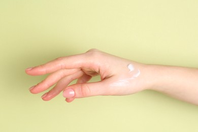 Photo of Woman with cream on her hand against green background, closeup