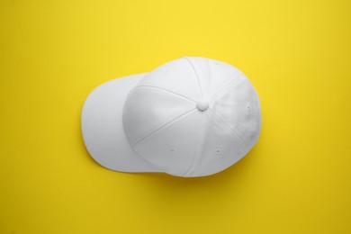 Stylish white baseball cap on yellow background, top view