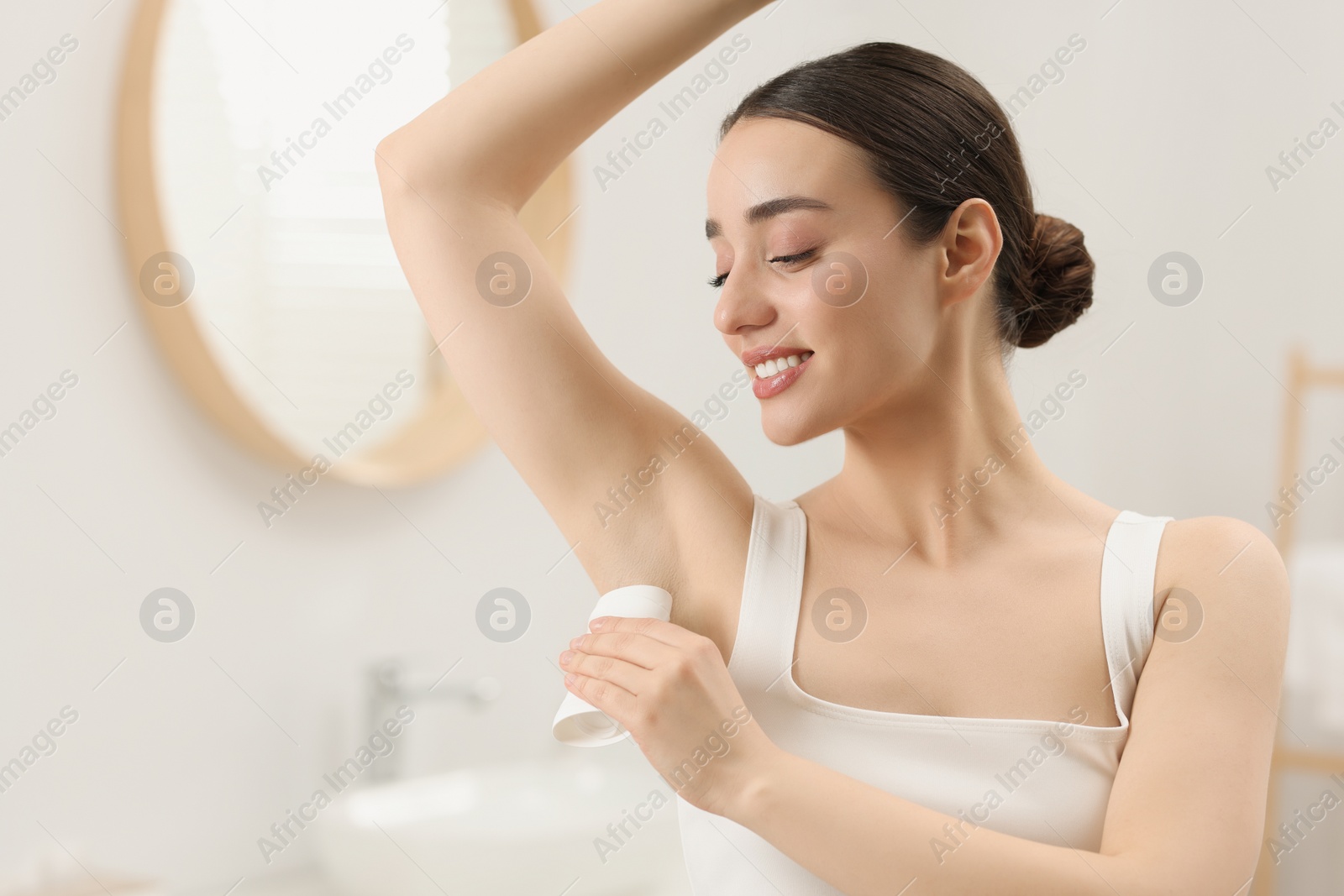 Photo of Beautiful young woman applying deodorant in bathroom