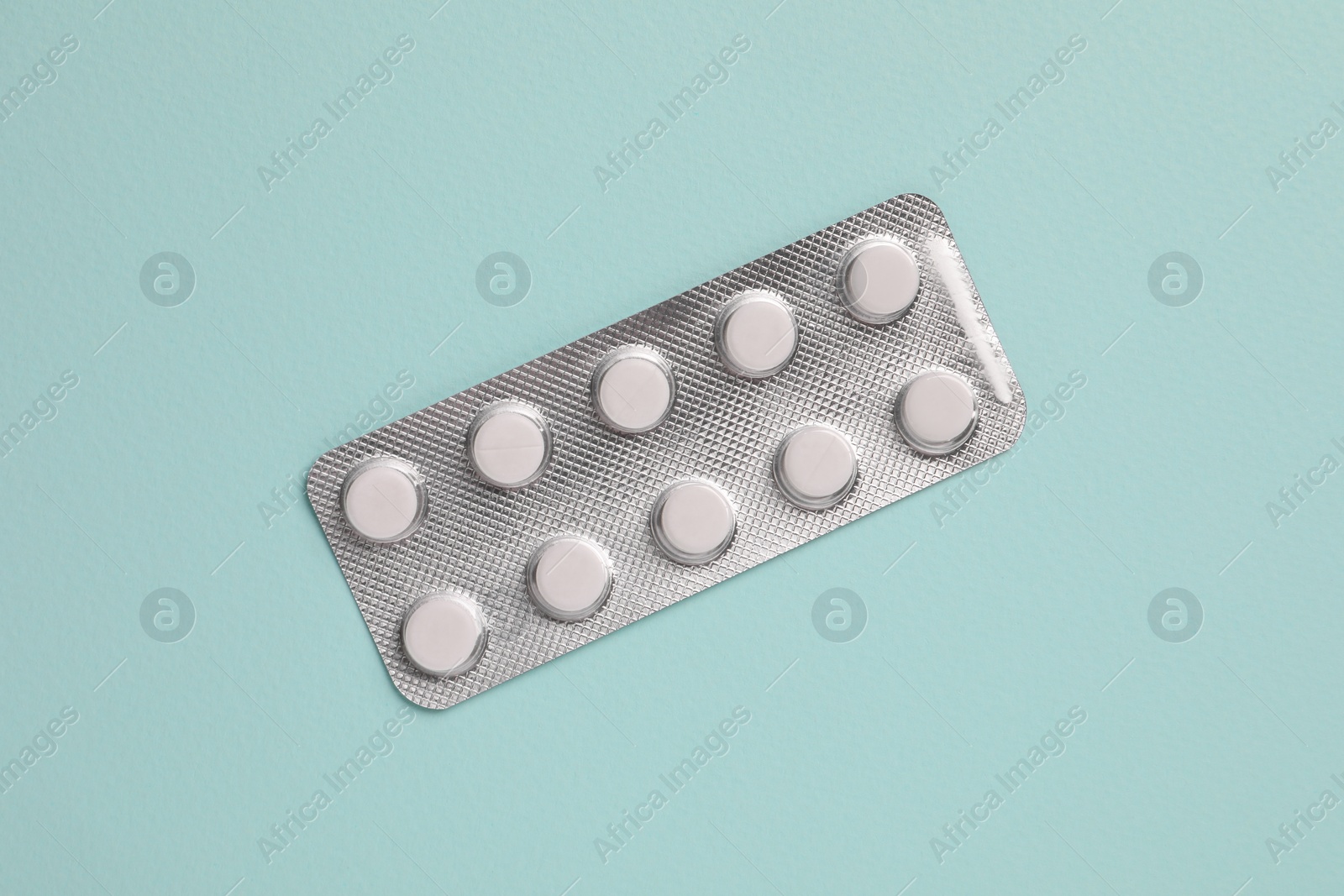 Photo of White pills in blister on pale green background, top view