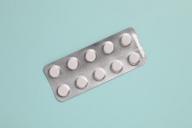 Photo of White pills in blister on pale green background, top view