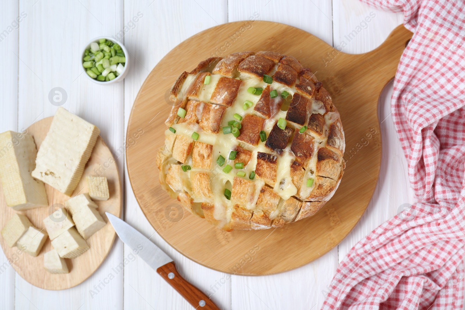 Photo of Freshly baked bread with tofu cheese, green onions and knife on white wooden table, flat lay