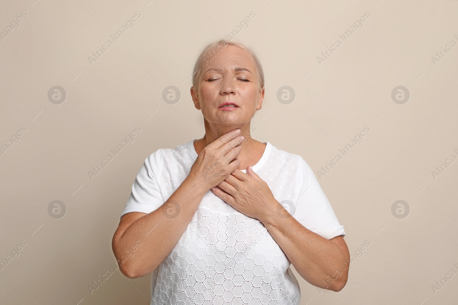 Photo of Mature woman doing thyroid self examination on beige background