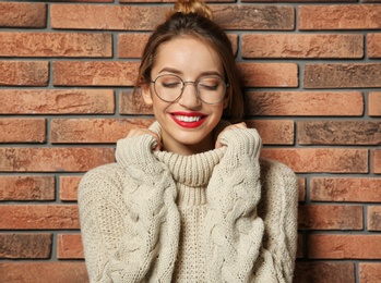 Beautiful young woman in warm sweater near brick wall