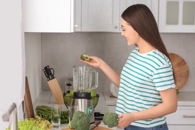 Photo of Woman adding broccoli into blender for smoothie in kitchen