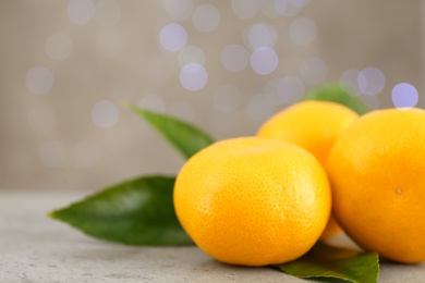 Photo of Tangerines with green leaves on grey table against blurred lights, space for text