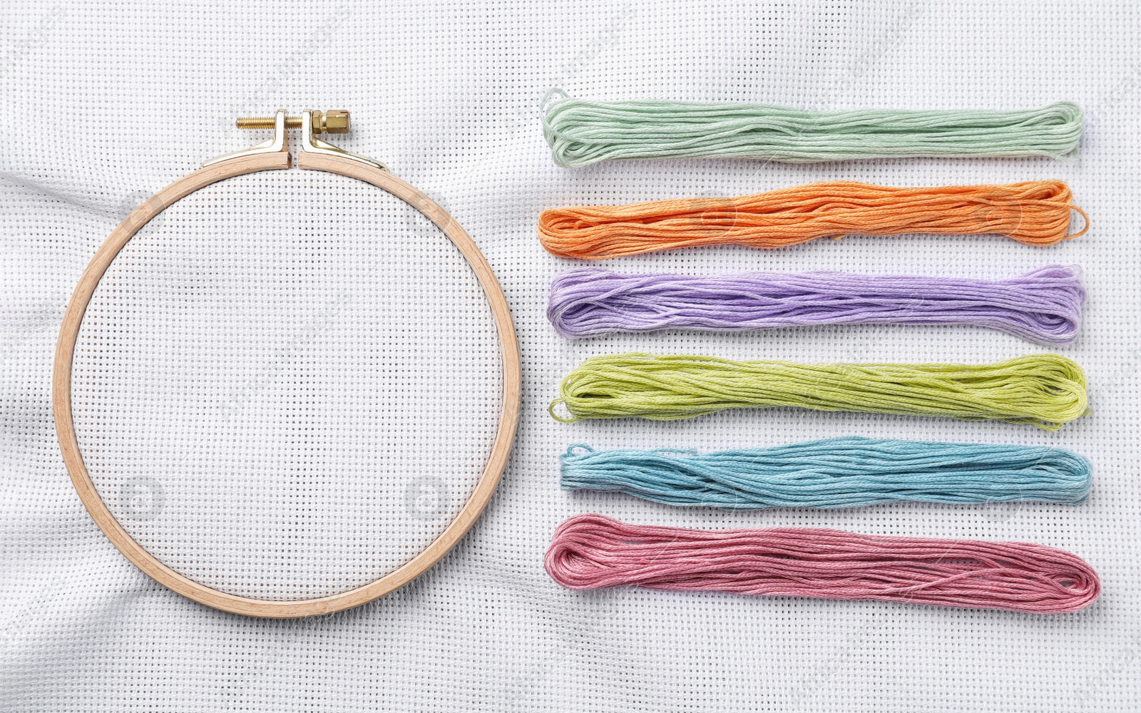 Photo of Threads near embroidery hoop with white fabric, flat lay