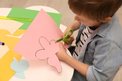 Little boy cutting color paper with scissors at table indoors