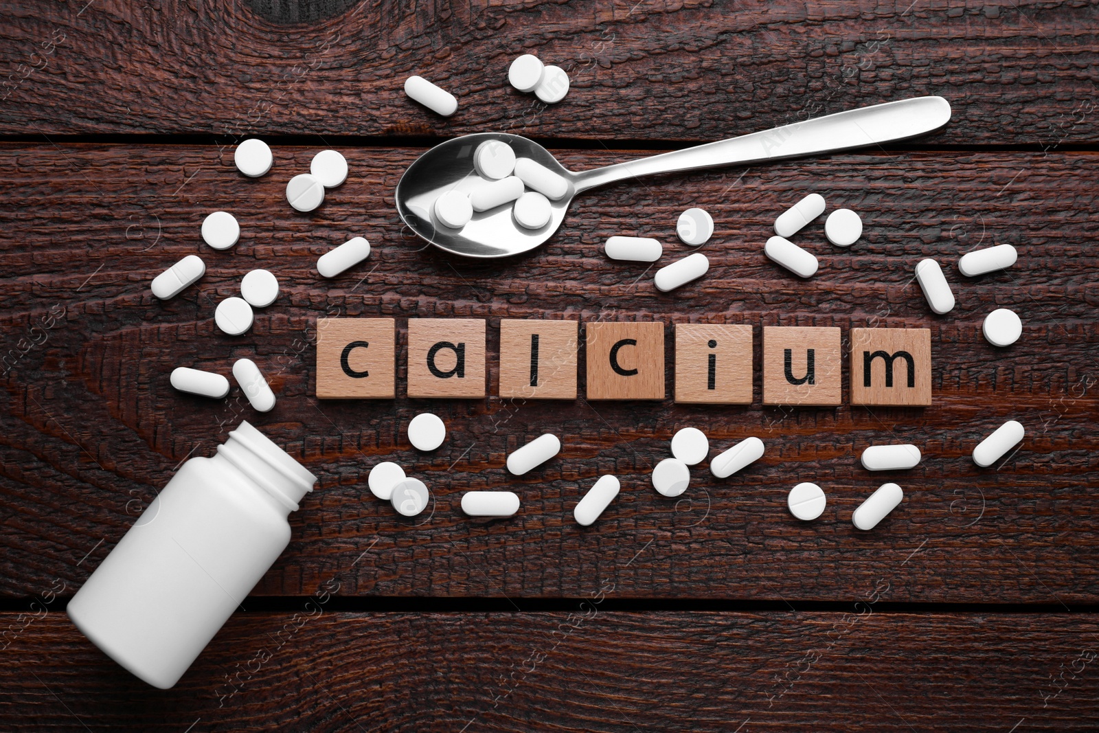 Photo of Word Calcium made of cubes with letters, spoon and pills on wooden table, top view