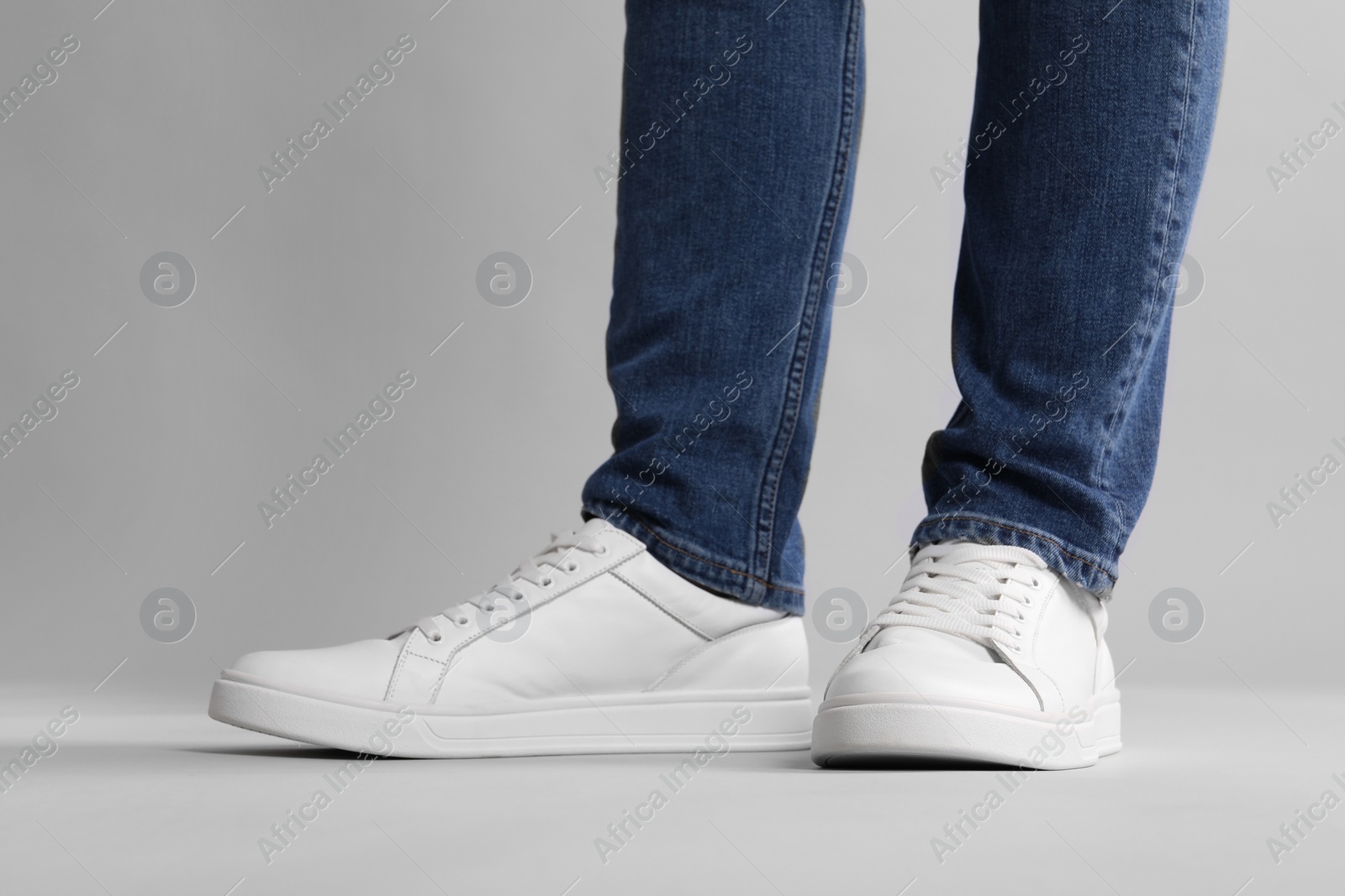 Photo of Man wearing stylish white sneakers on grey background, closeup