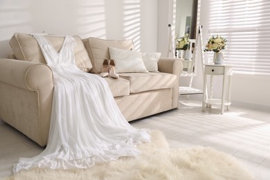 Beautiful wedding dress and shoes on sofa indoors