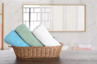 Image of Wicker basket with clean soft towels on wooden table in bathroom. Space for text