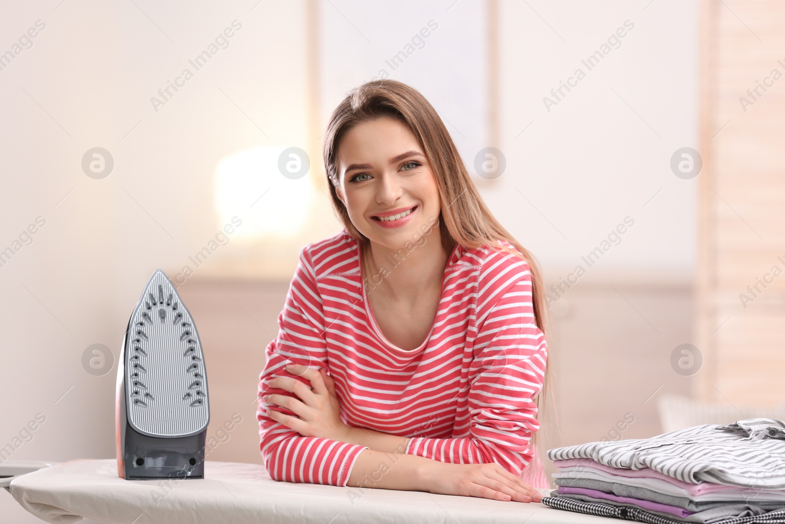 Photo of Young pretty woman with iron and clean laundry at board indoors