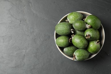 Photo of Fresh green feijoa fruits in bowl on black table, top view. Space for text