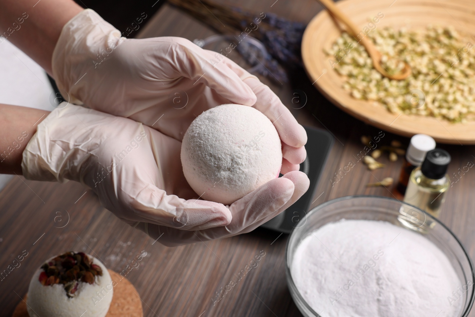 Photo of Woman holding handmade bath bomb above wooden table, closeup