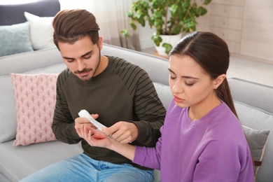 Young man applying bandage on woman's injured hand at home. First aid