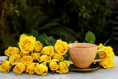 Cup of drink and beautiful yellow roses on light table outdoors, space for text