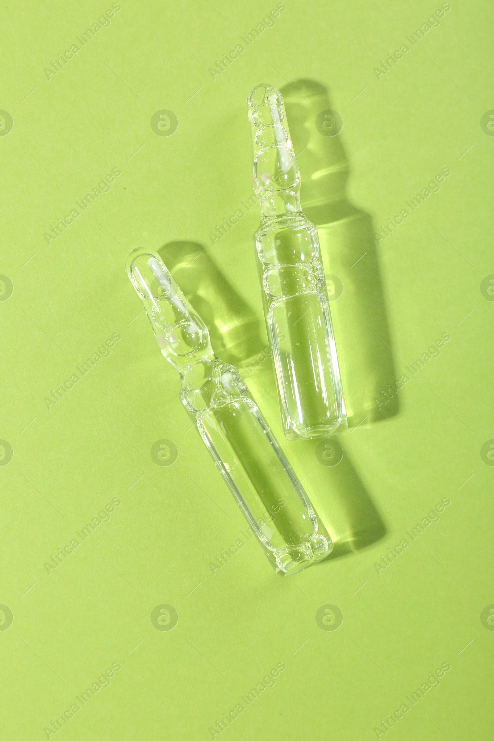 Photo of Glass ampoules with liquid on light green background, top view