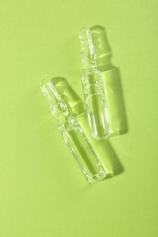 Glass ampoules with liquid on light green background, top view