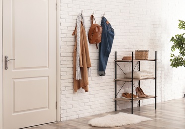 Photo of Stylish hallway interior with door, comfortable furniture and clothes on brick wall