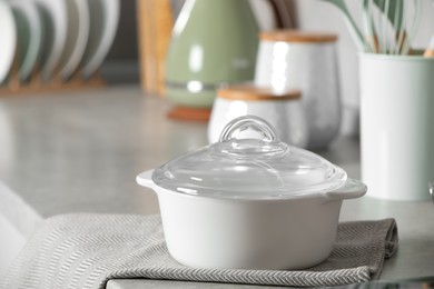 Ceramic pot with glass lid on light grey countertop in kitchen