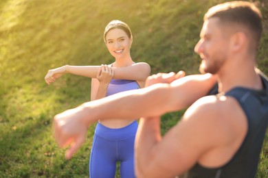 Photo of Attractive couple doing sports exercises in park on sunny day. Stretching outdoors