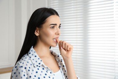 Photo of Young woman biting her nails at home. Space for text