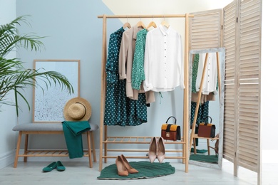 Photo of Wardrobe rack with women's clothes and shoes at color wall in room