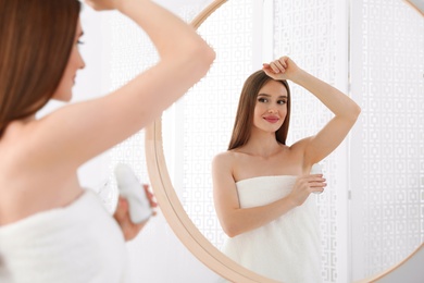 Beautiful young woman applying deodorant after shower in bathroom