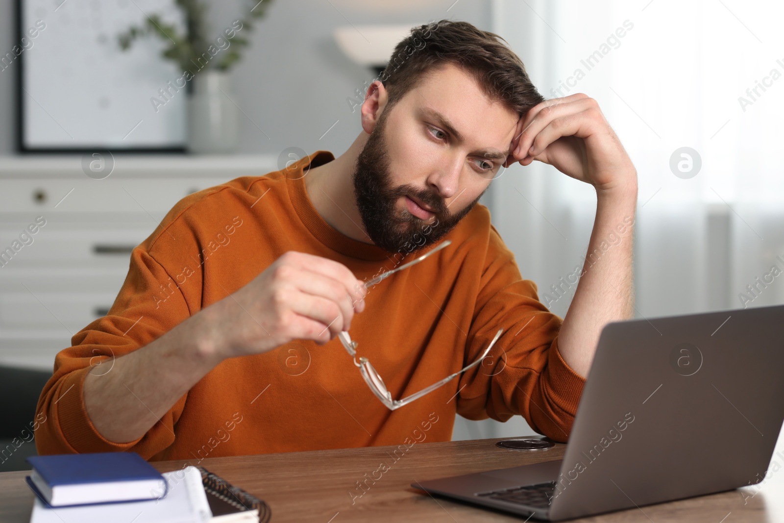 Photo of Overwhelmed man sitting with laptop at table indoors