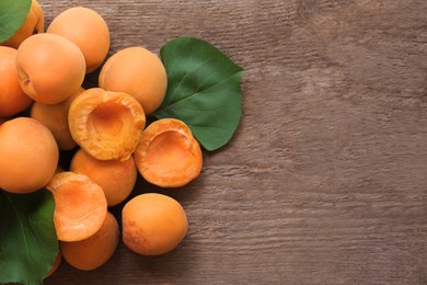 Delicious ripe apricots with green leaves on wooden table, top view. Space for text