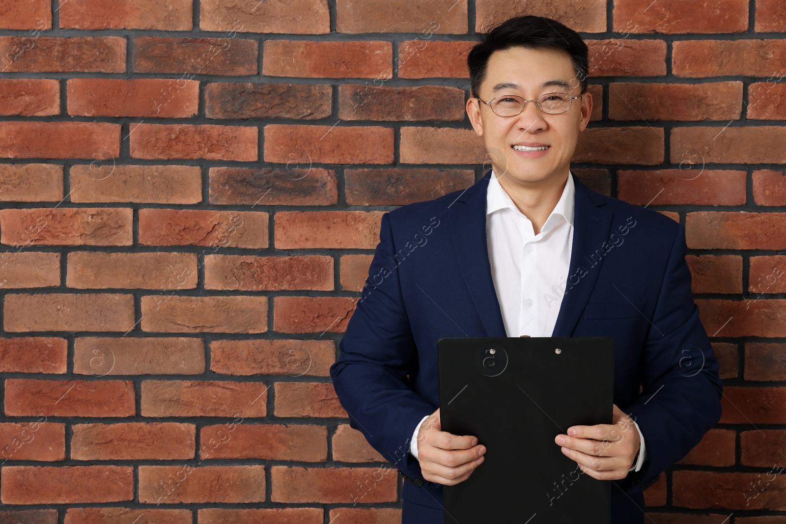 Photo of Happy boss with clipboard near brick wall. Space for text