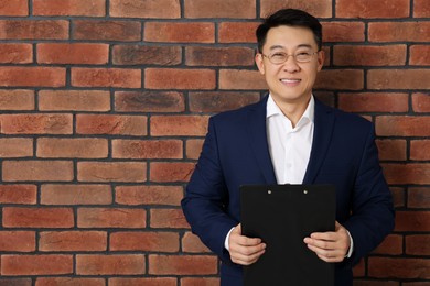 Photo of Happy boss with clipboard near brick wall. Space for text