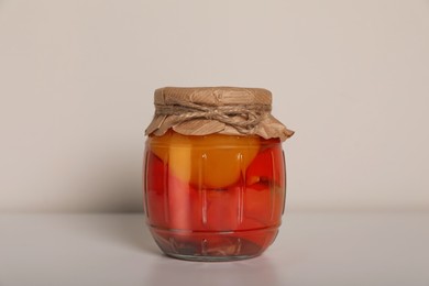 Photo of Jar of tasty pickled peppers on white table