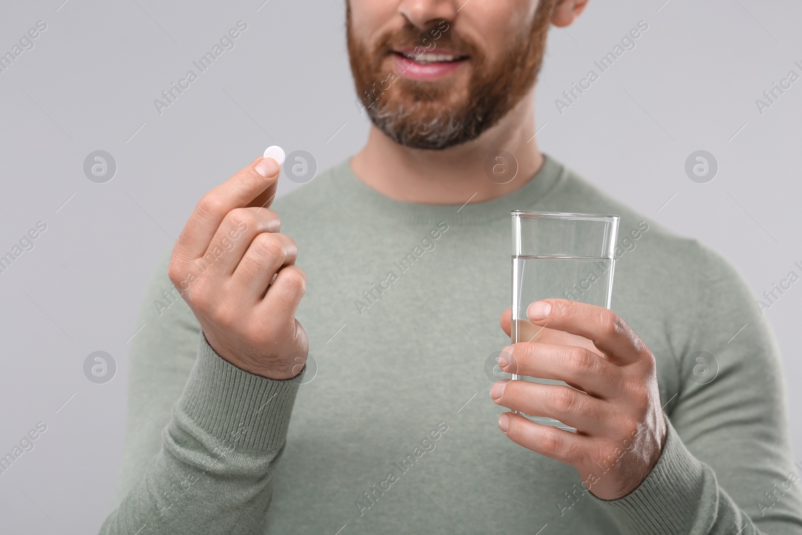 Photo of Man with glass of water and pill on light grey background, closeup